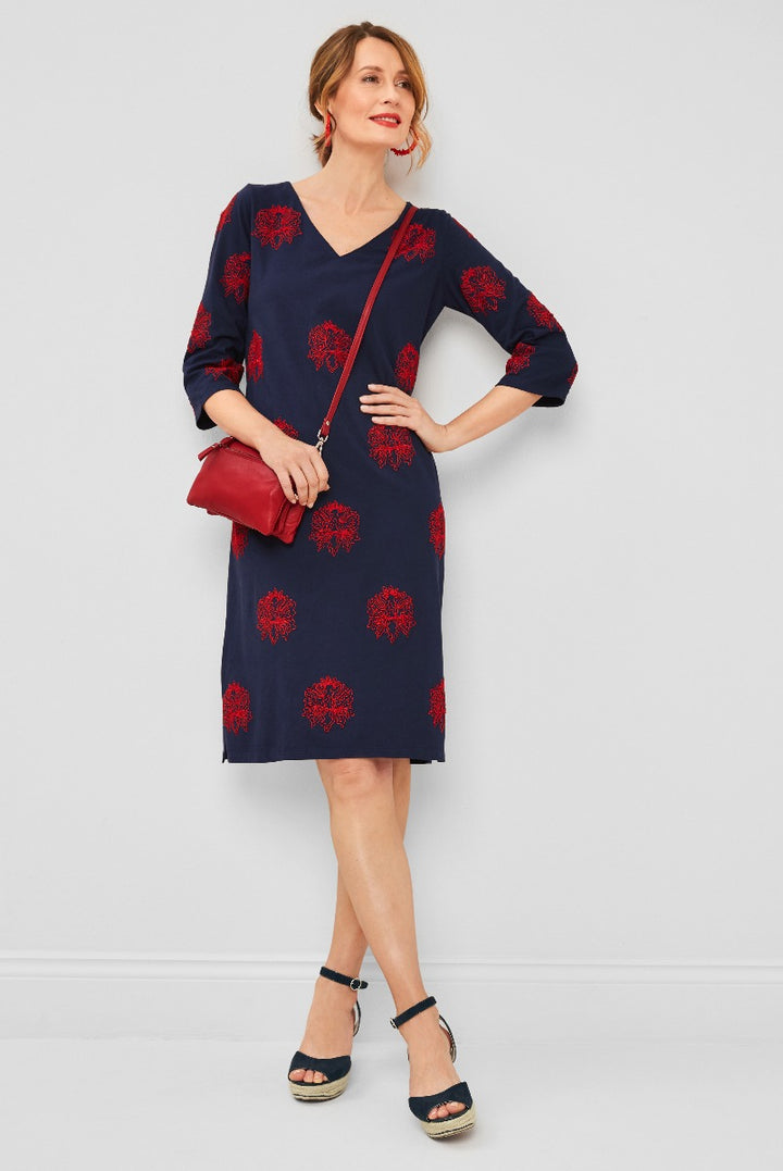 Lily Ella Collection elegant navy dress with red floral pattern, V-neck, three-quarter sleeves, paired with a red crossbody bag and navy ankle-strap wedge sandals.