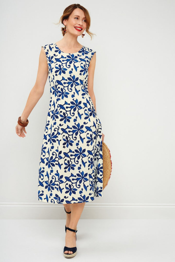 Lily Ella Collection elegant navy blue and white floral print A-line midi dress with sleeveless design, paired with stylish black strappy heels and a woven straw hat for a summer chic look.