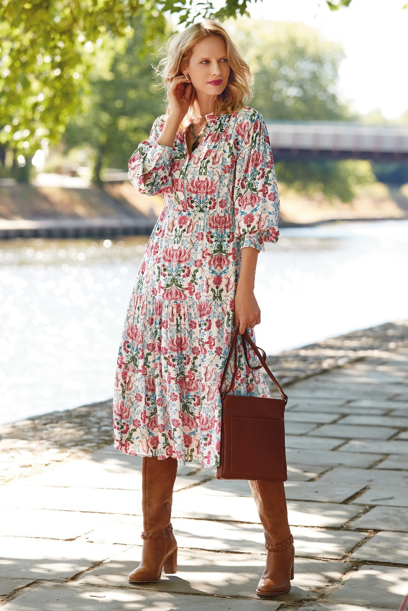 Lily Ella Collection floral print midi dress in pink and green, stylish woman walking by river, accessorized with brown leather boots and tote bag