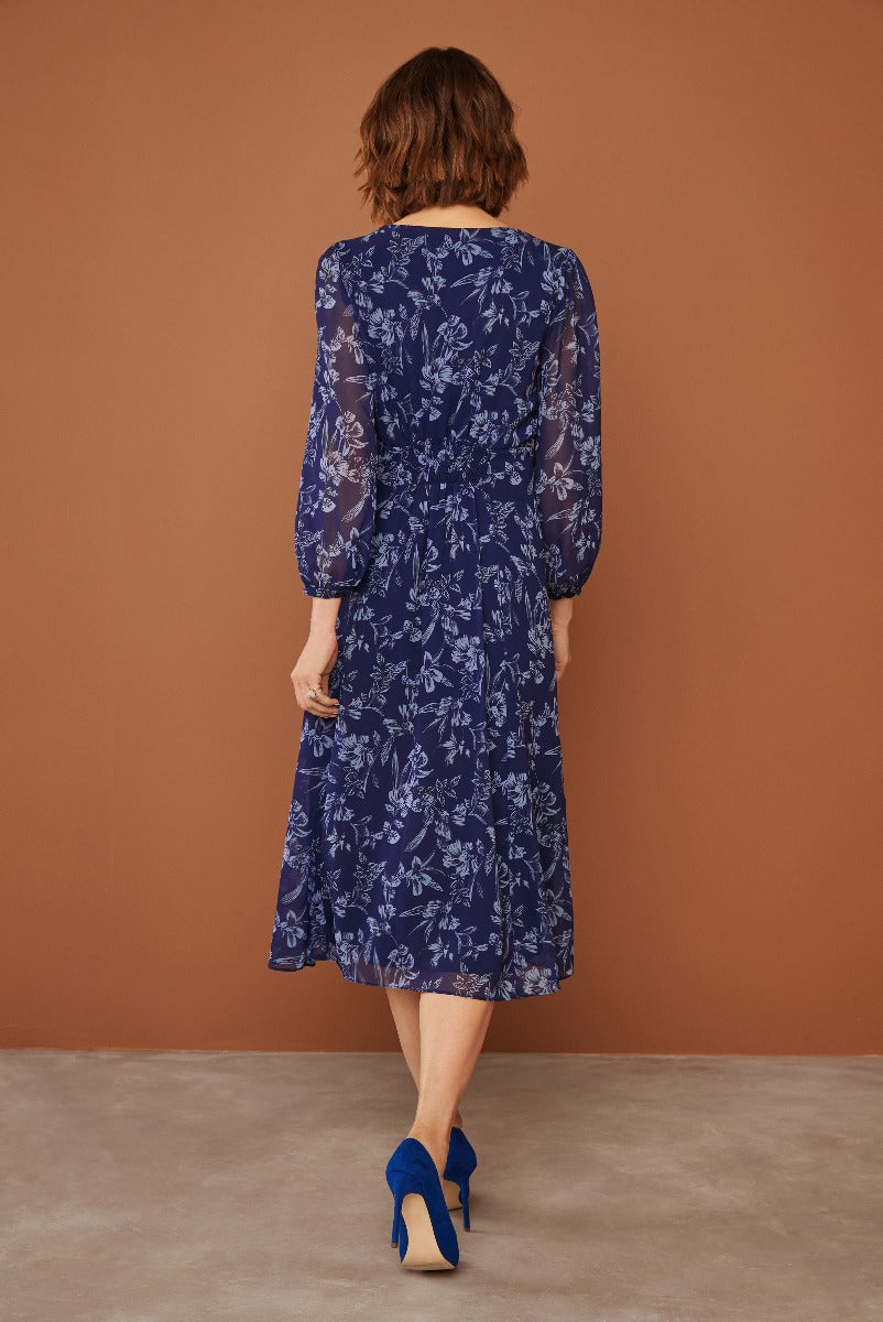 Lily Ella Collection navy blue floral dress with sheer sleeves and elegant mid-length cut paired with stylish blue heels for a sophisticated women's fashion look.