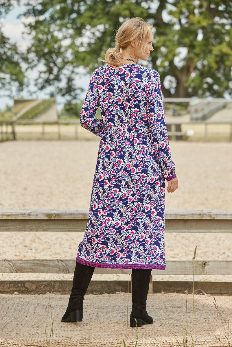 Woman wearing Lily Ella Collection long-sleeve navy dress with floral paisley pattern, styled with black knee-high boots, outdoor setting.