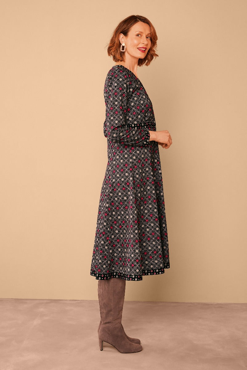 Lily Ella Collection black floral mid-length dress with three-quarter sleeves paired with taupe suede boots on model against a beige background.