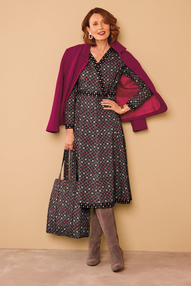 Lily Ella Collection elegant fuchsia coat over black patterned dress with matching tote and grey boots on a model