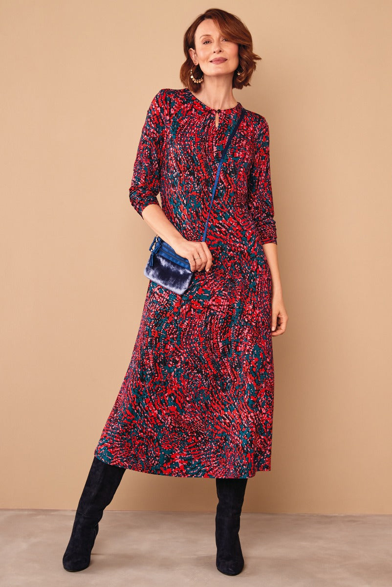 Lily Ella Collection red and blue patterned midi dress with tassel neck detail, model holding blue velvet clutch, paired with black suede boots, elegant women's fashion.