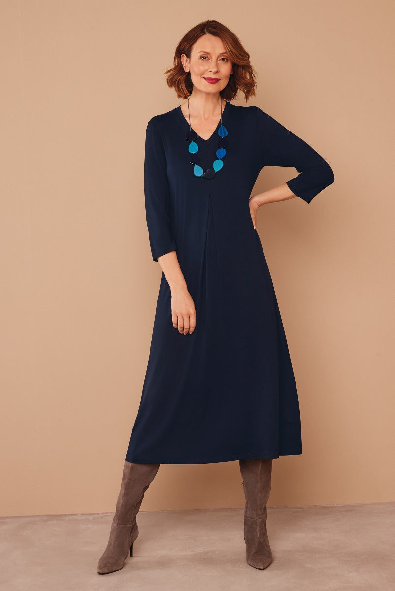 Lily Ella Collection navy blue midi dress with three-quarter sleeves and statement necklace, elegant women's fashion, model wearing stylish autumn dress with knee-high suede boots.