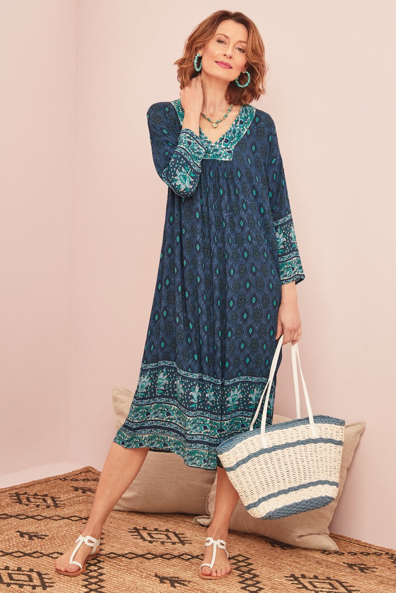 Lily Ella Collection bohemian style teal patterned dress with white sandals and striped tote bag for spring and summer fashion.