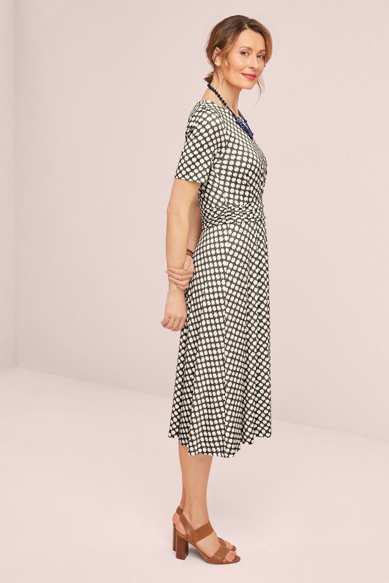 Lily Ella Collection elegant black and white geometric pattern midi dress, stylish short-sleeve design with v-neckline and wrap waist, paired with brown heeled sandals, perfect sophisticated outfit for mature women.