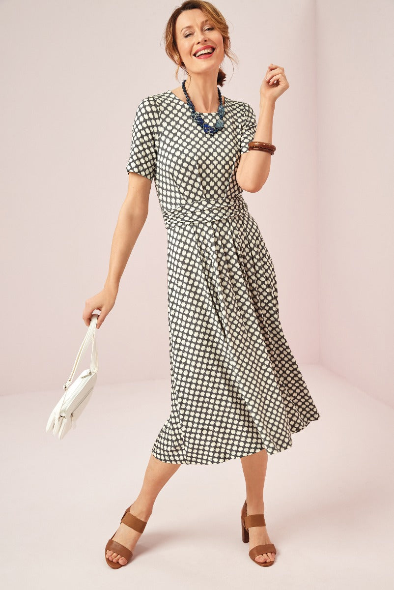 Lily Ella Collection black and white patterned wrap dress, stylish midi length with short sleeves, paired with brown sandals and white handbag, showcasing modern elegance for women.