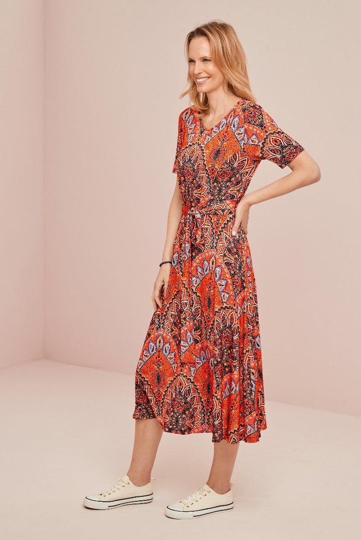 Lily Ella Collection mid-length bohemian style patterned dress in vibrant orange tones, paired with casual white sneakers, showcasing contemporary feminine fashion.