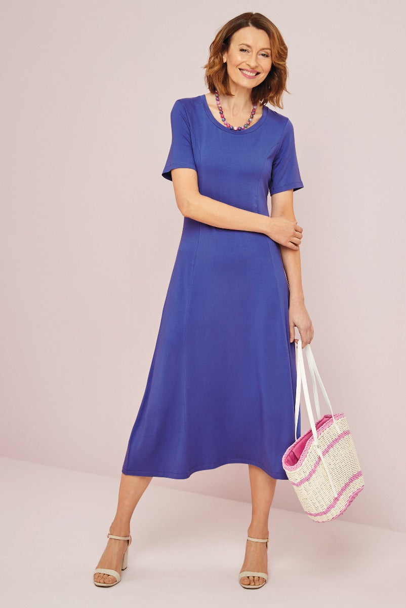 Lily Ella Collection elegant royal blue midi dress with short sleeves, summer fashion, woman smiling and posing with a woven tote bag and beige sandals