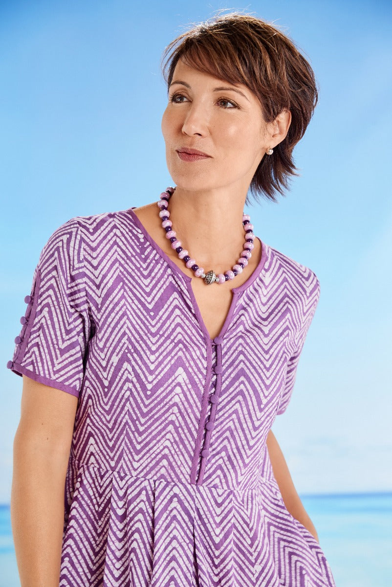 Lily Ella Collection chevron pattern purple dress with short sleeves and button details, accessorized with purple bead necklace, women's fashion on beach background
