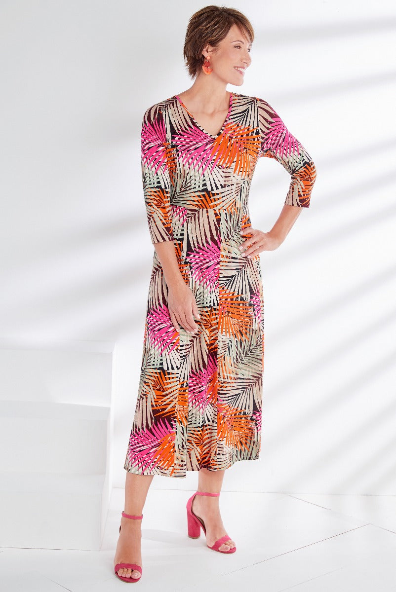 Lily Ella Collection vibrant orange-pink patterned midi dress with three-quarter sleeves and V-neck, paired with matching statement earrings and pink heeled sandals.