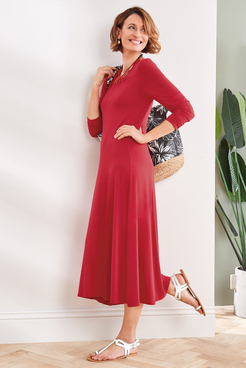 Lily Ella Collection elegant red midi dress with three-quarter sleeves and flared hem, woman posing with a natural straw bag and white sandals, stylish and comfortable daywear