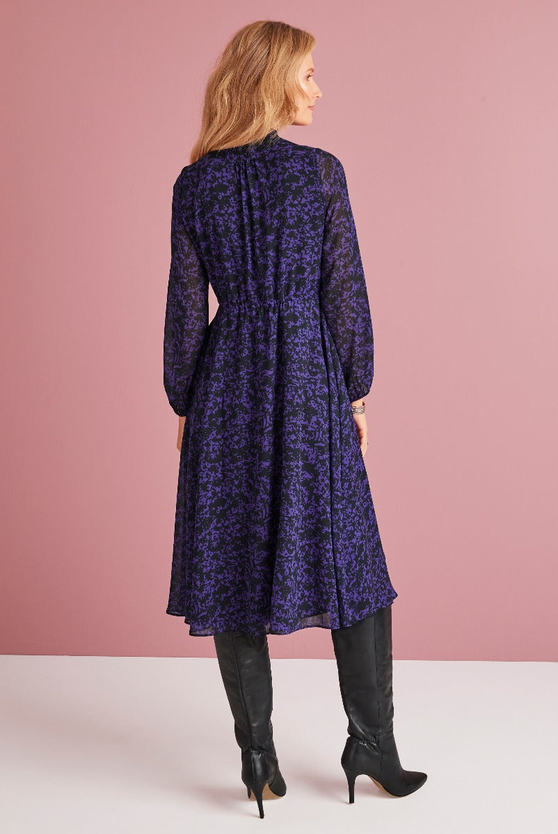 Lily Ella Collection elegant purple floral pattern midi dress with full sleeves and high black boots, fashionable women's clothing rear view.