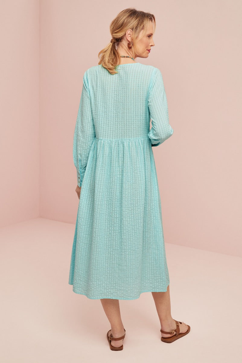 Lily Ella Collection aqua blue textured midi dress with long sleeves and gathered waistline, model showcasing women's casual elegant fashion from the back, paired with brown sandals.
