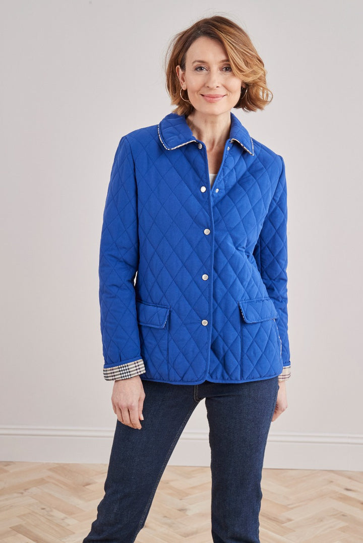 Lily Ella Collection elegant royal blue quilted jacket for women, styled with contrasting white buttons and gingham cuff details, paired with dark denim jeans