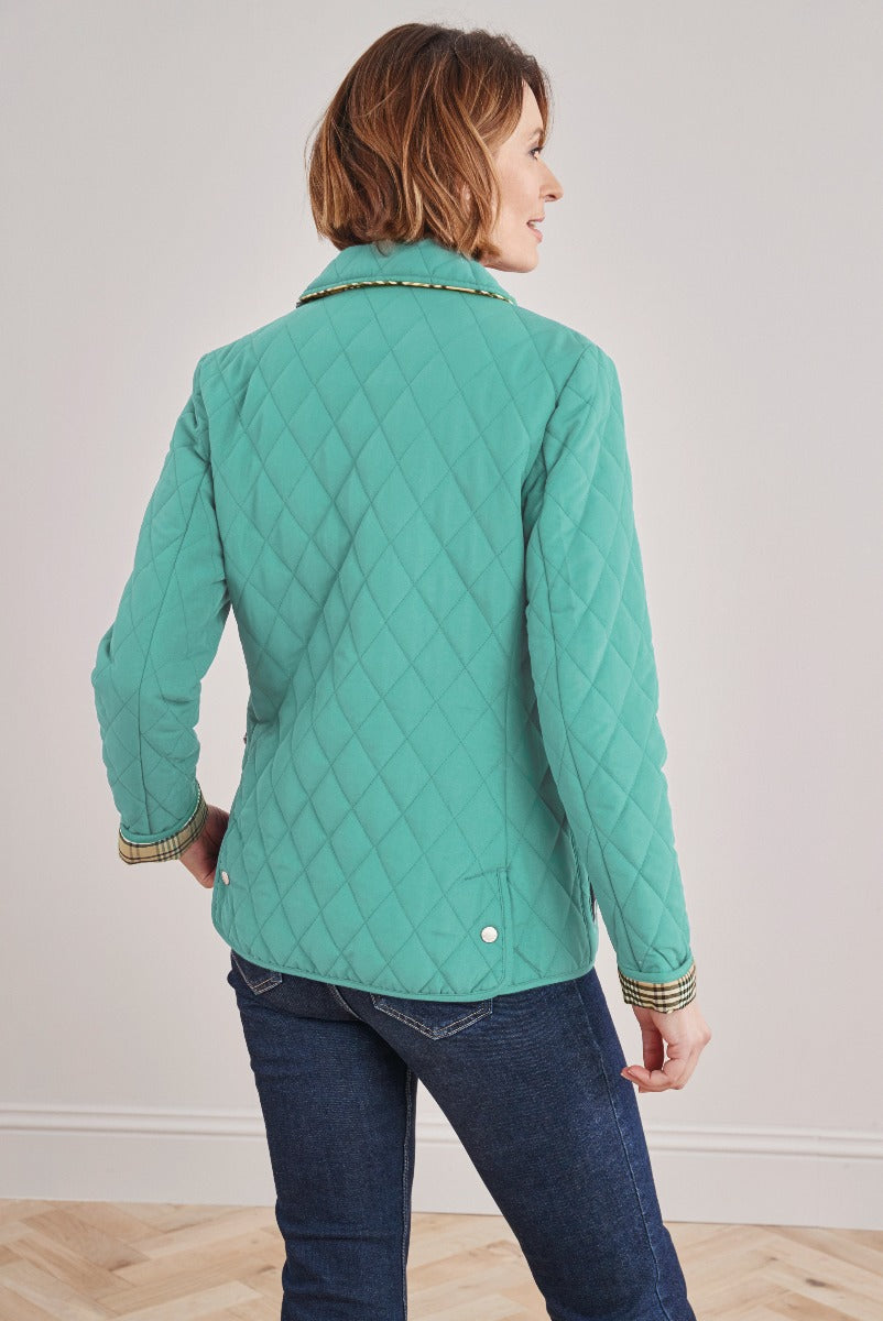 Lily Ella Collection teal quilted jacket, contemporary womenswear, stylish diamond-patterned outerwear, with detailed cuffs, paired with classic denim jeans, rear view.