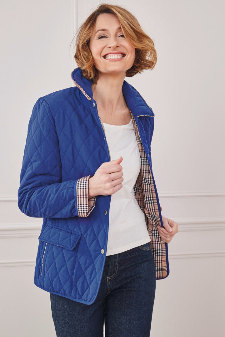 Lily Ella Collection women's royal blue quilted jacket, chic outerwear with plaid lining, paired with white top and denim jeans.