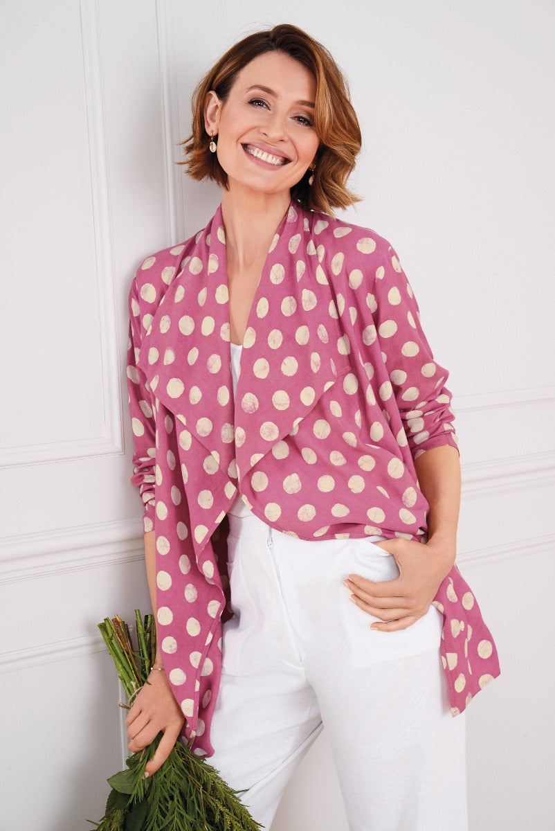 Lily Ella Collection stylish woman in magenta and cream polka dot blouse with white trousers holding a bouquet of greenery.