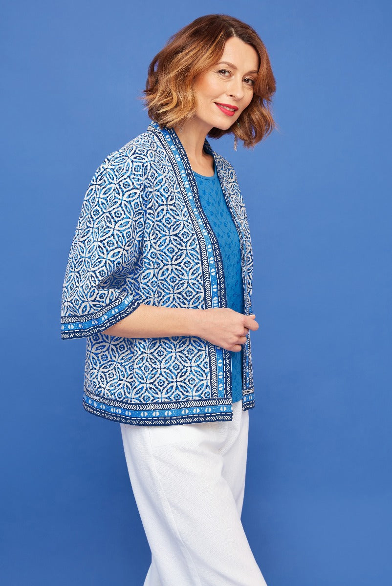 Lily Ella Collection blue and white patterned jacket with matching top and white trousers on a model against blue background.