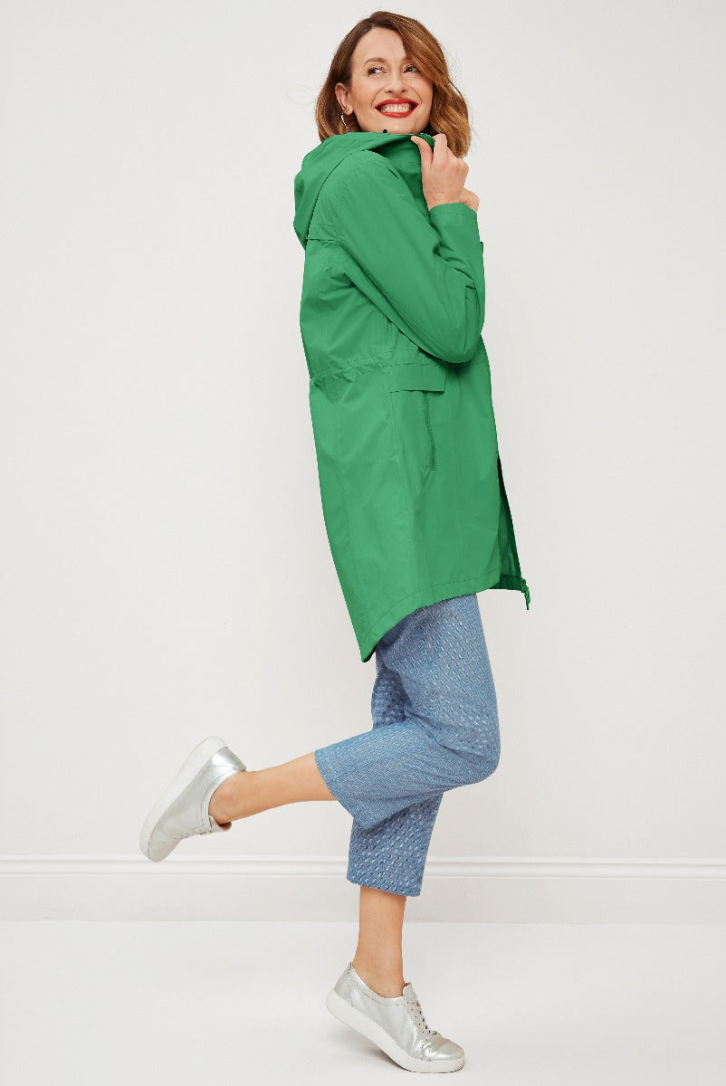 Lily Ella Collection stylish green parka jacket for women, casual blue trousers, silver sneakers, trendy spring outerwear fashion, upbeat female model posing