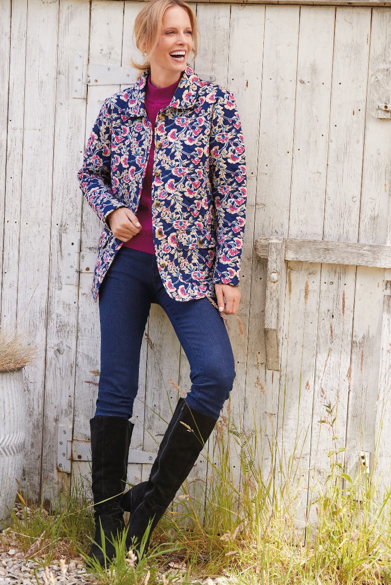 Lily Ella Collection navy blue floral quilted jacket paired with slim-fit jeans and black knee-high boots, woman posing against rustic wooden background.