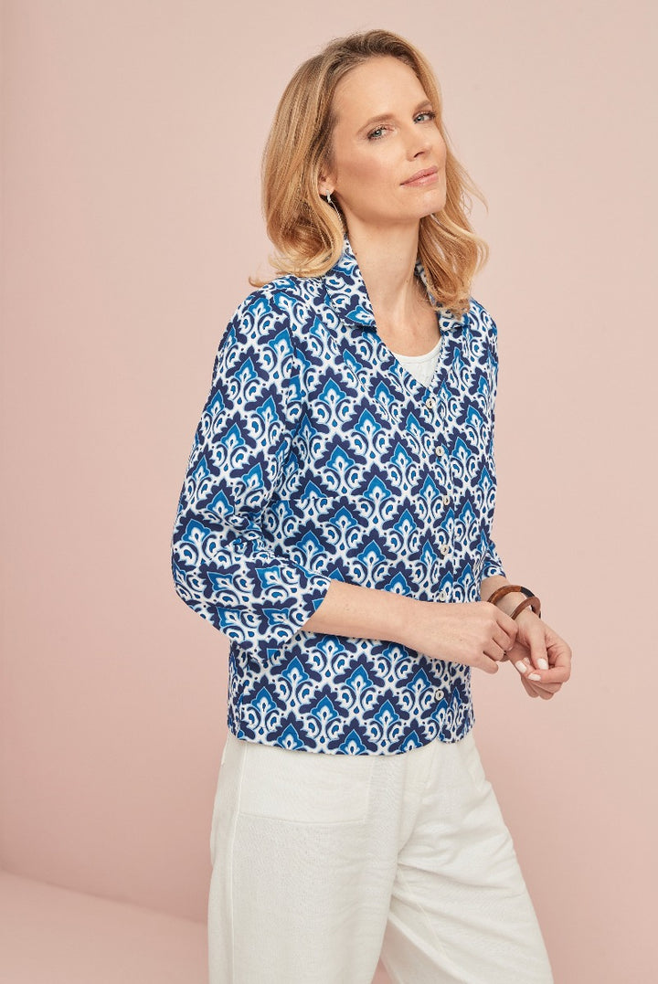 Lily Ella Collection model showcasing blue and white patterned blouse with a stylish v-neck cut and three-quarter sleeves, paired with white trousers for a fresh, sophisticated look.
