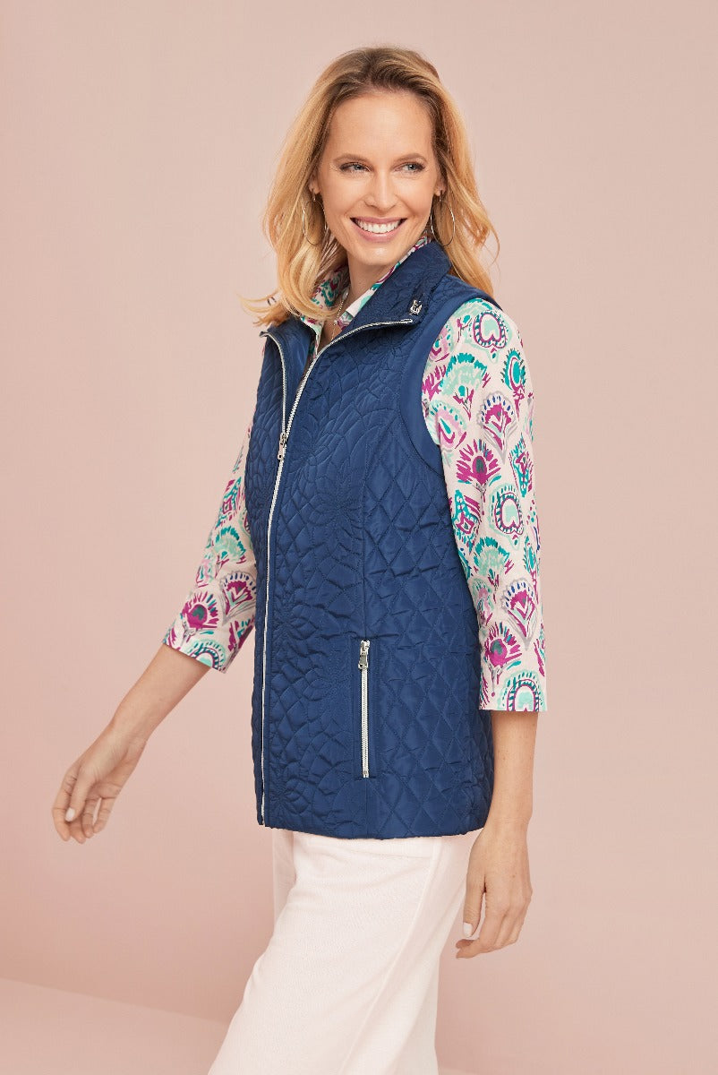 Lily Ella Collection navy blue quilted zip-up gilet with colorful paisley print lining modeled with white trousers for a chic, casual look.