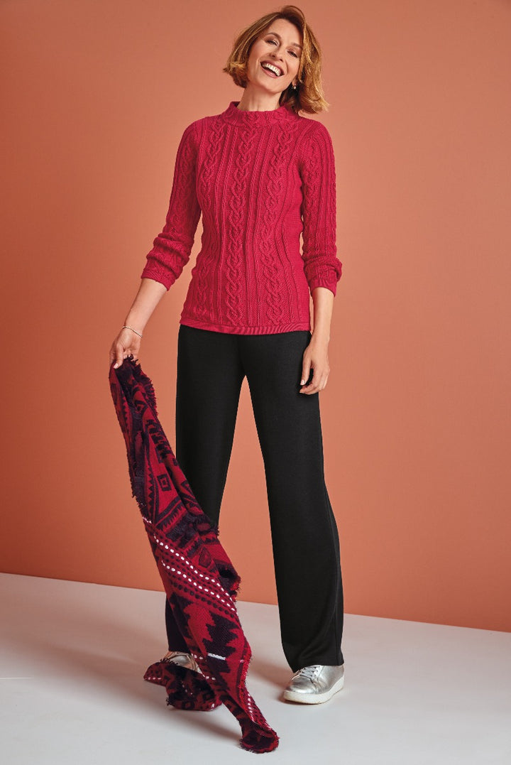 Lily Ella Collection vibrant red cable knit jumper, smiling woman model, stylish black trousers, patterned burgundy scarf accessory, fashionable silver shoes, contemporary autumn fashion look