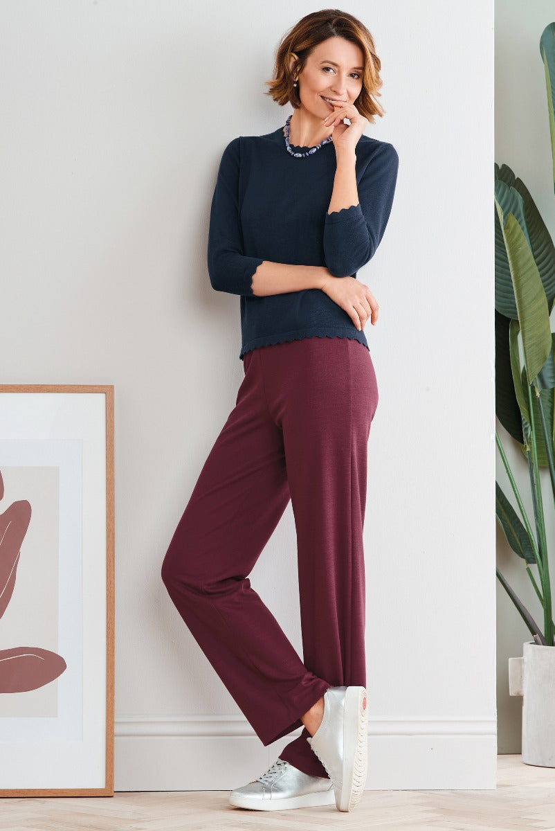 Lily Ella Collection women's fashion with model wearing a stylish navy blue sweater and burgundy trousers, paired with silver sneakers, casual chic attire in a modern interior setting.