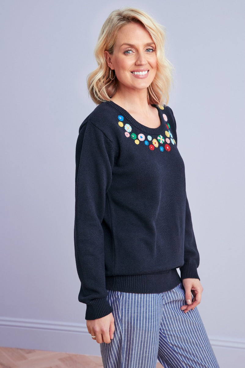 Lily Ella Collection navy blue jumper with colorful embroidered flowers, casual chic women's knitwear, paired with striped trousers.