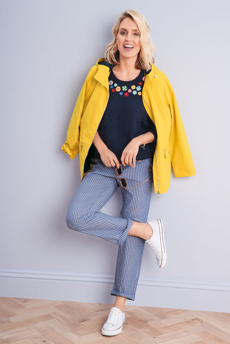 Lily Ella Collection chic casual outfit featuring a vibrant yellow raincoat, navy floral embroidered knitwear, and pinstripe blue trousers paired with white sneakers.