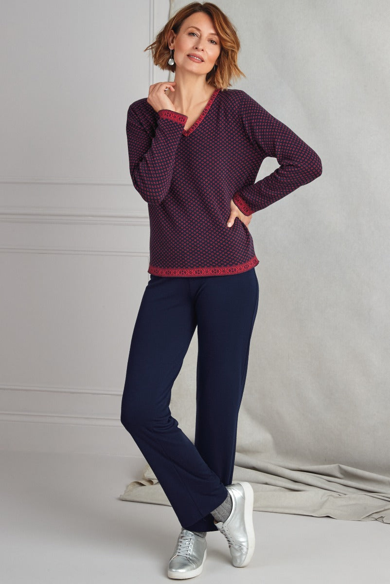 Lily Ella Collection stylish woman in navy and red patterned top with trim detail and slim navy trousers, paired with metallic silver sneakers for a casual chic look.
