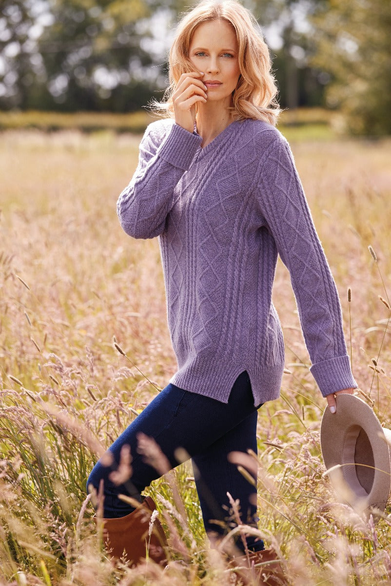 Lily Ella Collection elegant lavender cable knit sweater paired with navy leggings, woman holding a beige fedora, chic autumn outdoor fashion.