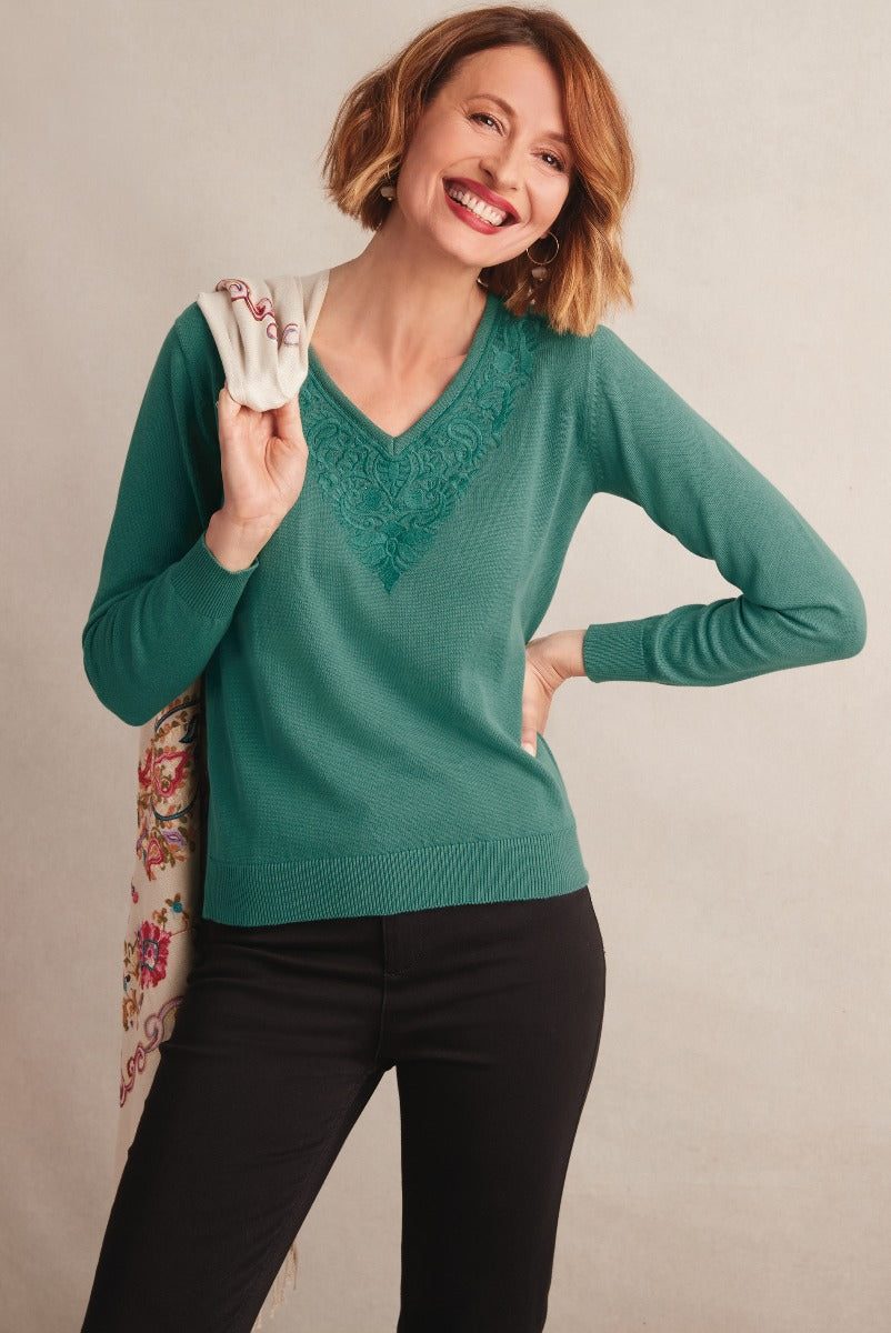 Lily Ella Collection emerald green V-neck jumper with lace detailing, stylish woman carrying embroidered shawl, posing with a smile, fashionable clothing for women, elegant casual outfit