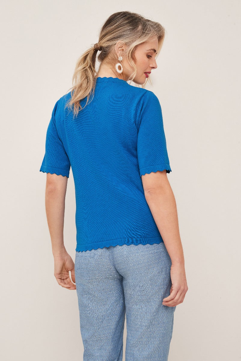 Lily Ella Collection vibrant blue knit top with scalloped hem and sleeve details, paired with casual light blue trousers, showcasing back view of elegant women's fashion.