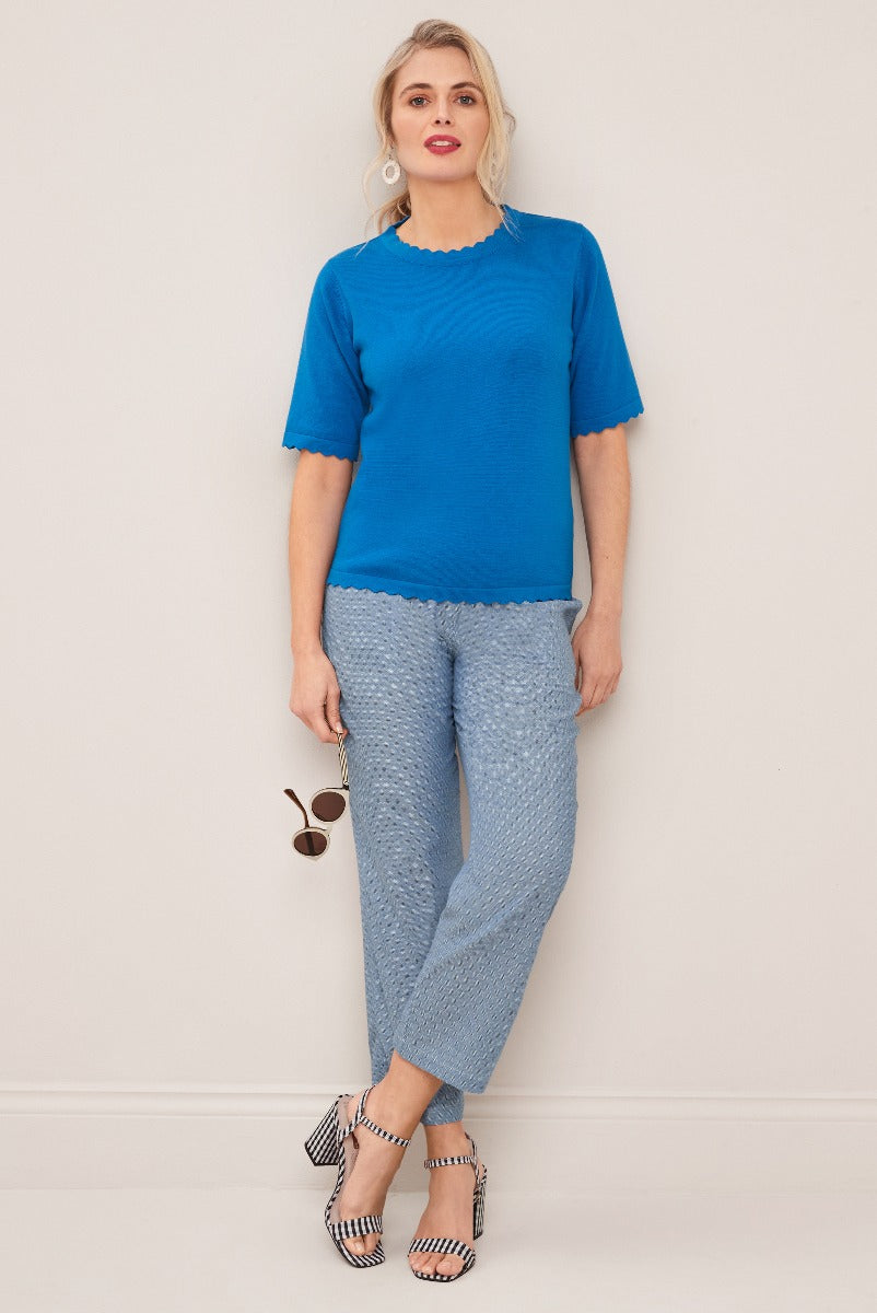 Lily Ella Collection vibrant blue scalloped-edge top paired with light blue textured trousers, stylish striped heels, and round sunglasses, showcasing elegant women's spring fashion.