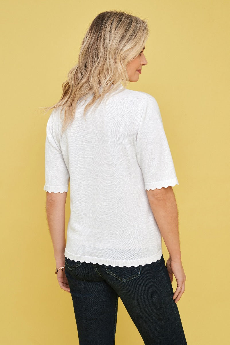 Lily Ella Collection white scallop-edged summer sweater, elegant short-sleeve knit top, paired with dark jeans on a yellow background.