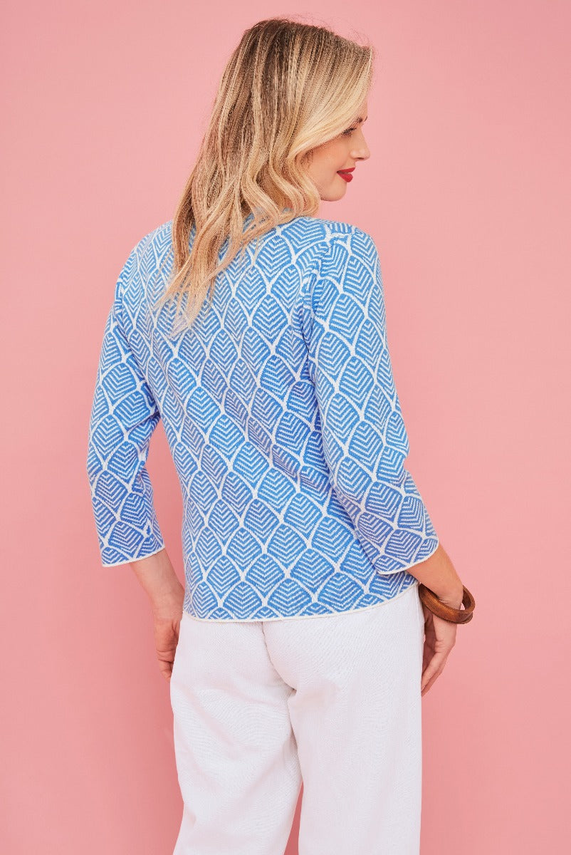 Lily Ella Collection blue geometric pattern blouse, stylish 3/4 sleeve top, elegant women's fashion, model posing in white trousers, pink background