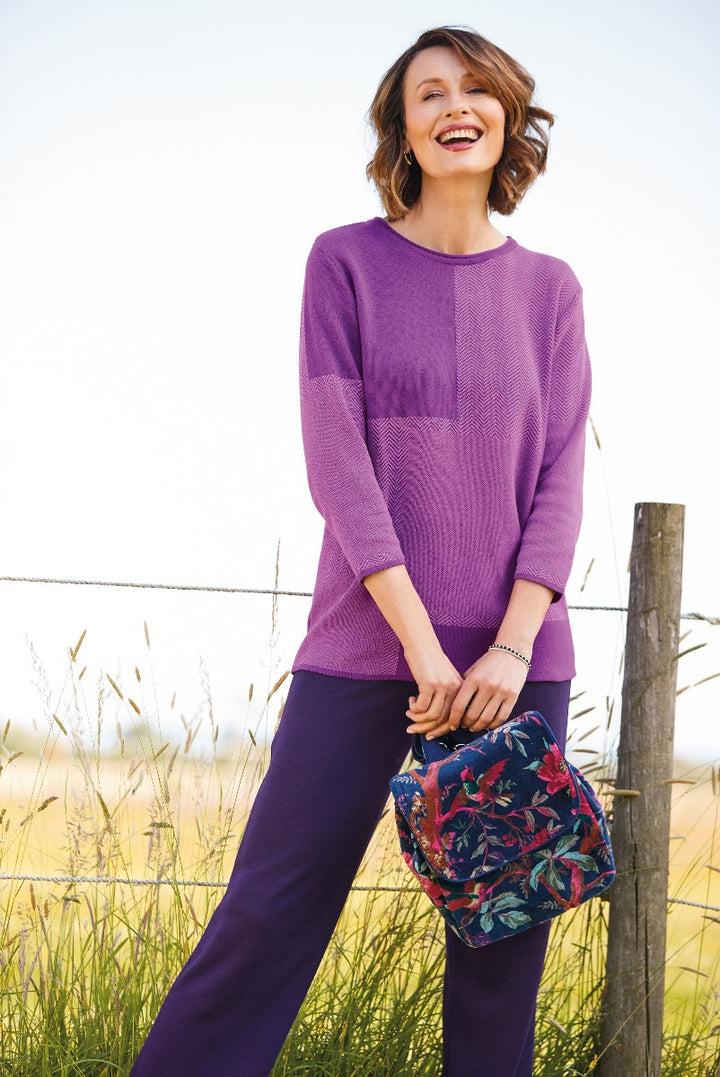 Lily Ella Collection vibrant purple textured jumper and coordinating trousers, stylish woman casual outdoor look with floral clutch accessory