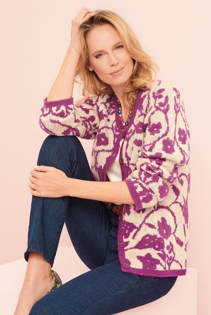 Lily Ella Collection purple floral pattern cardigan, stylish women's knitwear, model posing with denim jeans and colorful bead necklace against pink background.
