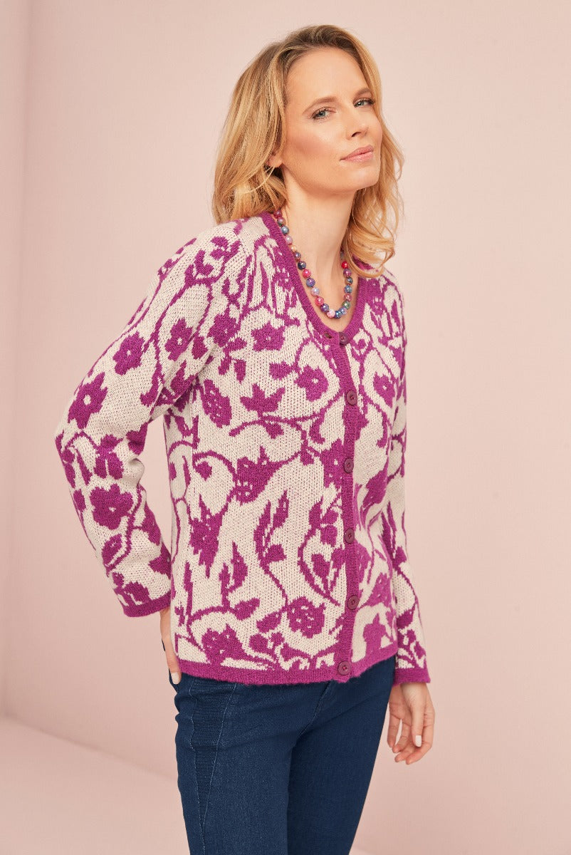 Lily Ella Collection stylish purple floral pattern cardigan, fashionable women's knitwear with button-up front, paired with blue jeans against a pastel pink background.