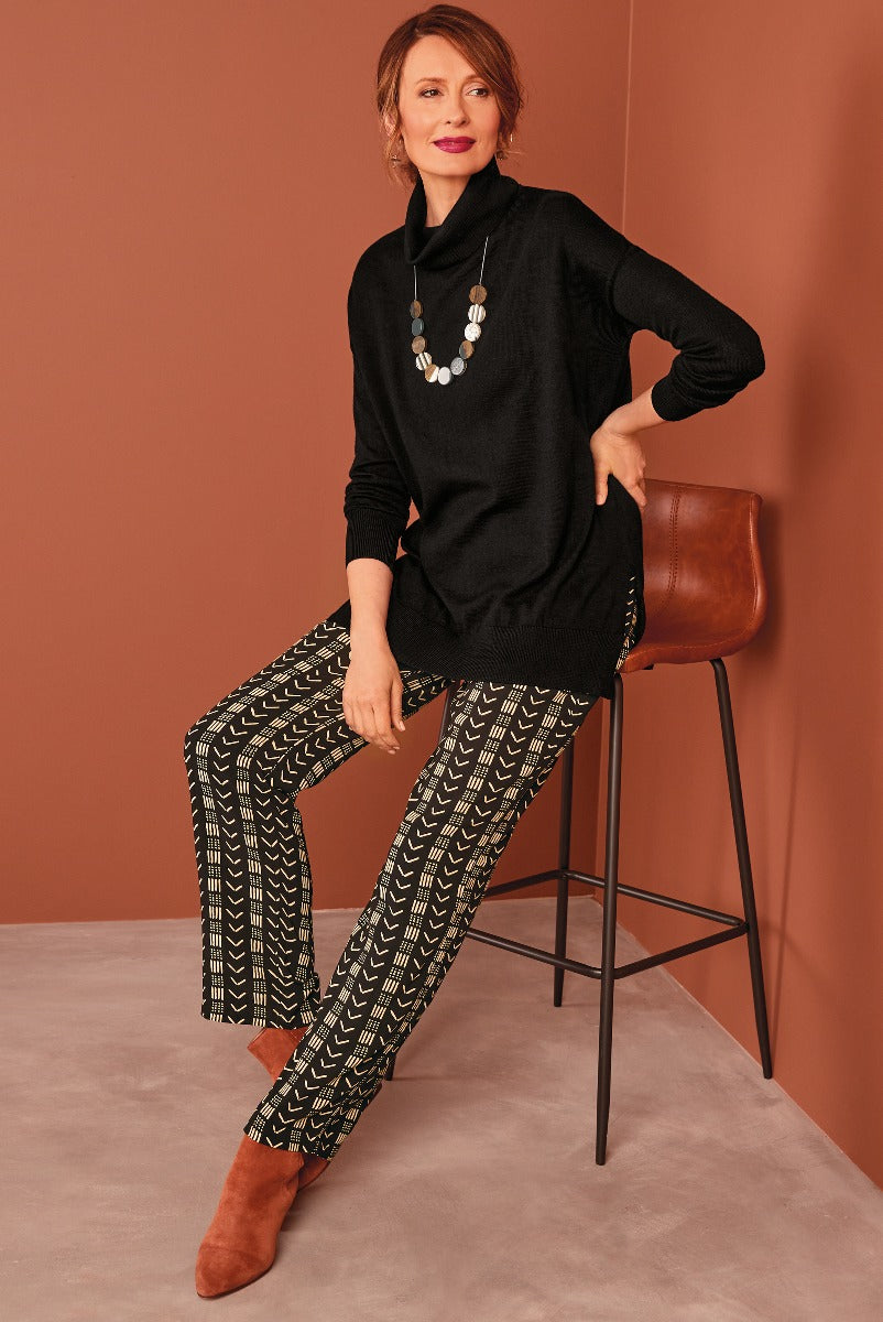 Lily Ella Collection elegant black tunic sweater with stylish geometric patterned trousers and brown ankle boots, accessorized with statement necklace, for a chic and sophisticated women's fashion look.