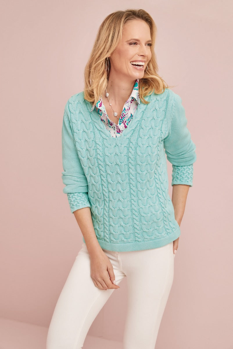 Lily Ella Collection aqua blue cable knit sweater, stylish women's casual wear paired with white trousers, laughing model showcasing contemporary fashion.