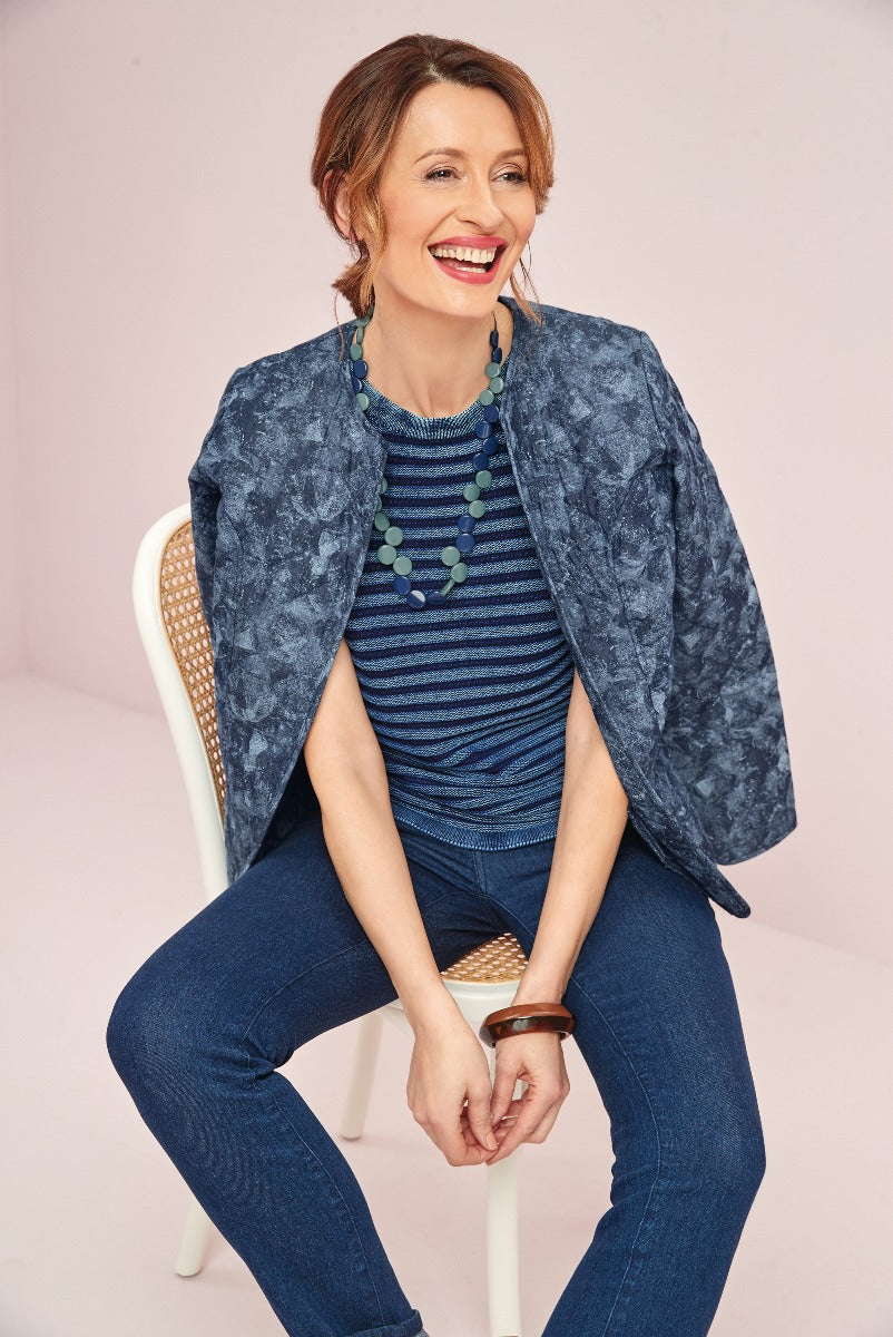 Lily Ella Collection casual style with smiling woman wearing blue textured jacket, striped blue top, navy jeans and teal bead necklace.