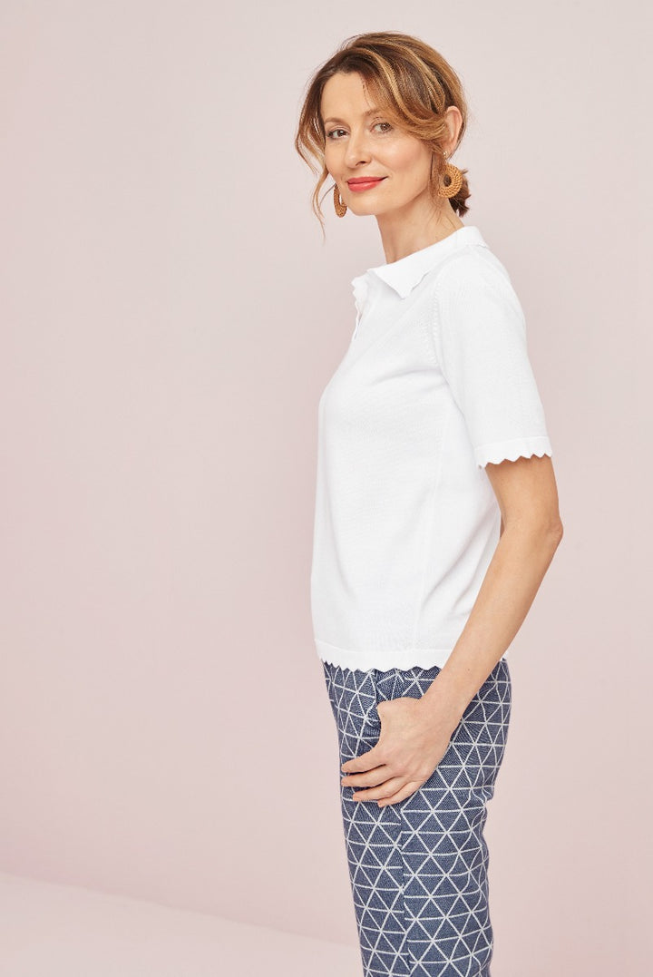 Lily Ella Collection white scalloped hem top and printed navy trousers, elegant casual women's apparel, stylish mature female model posing against pink background.