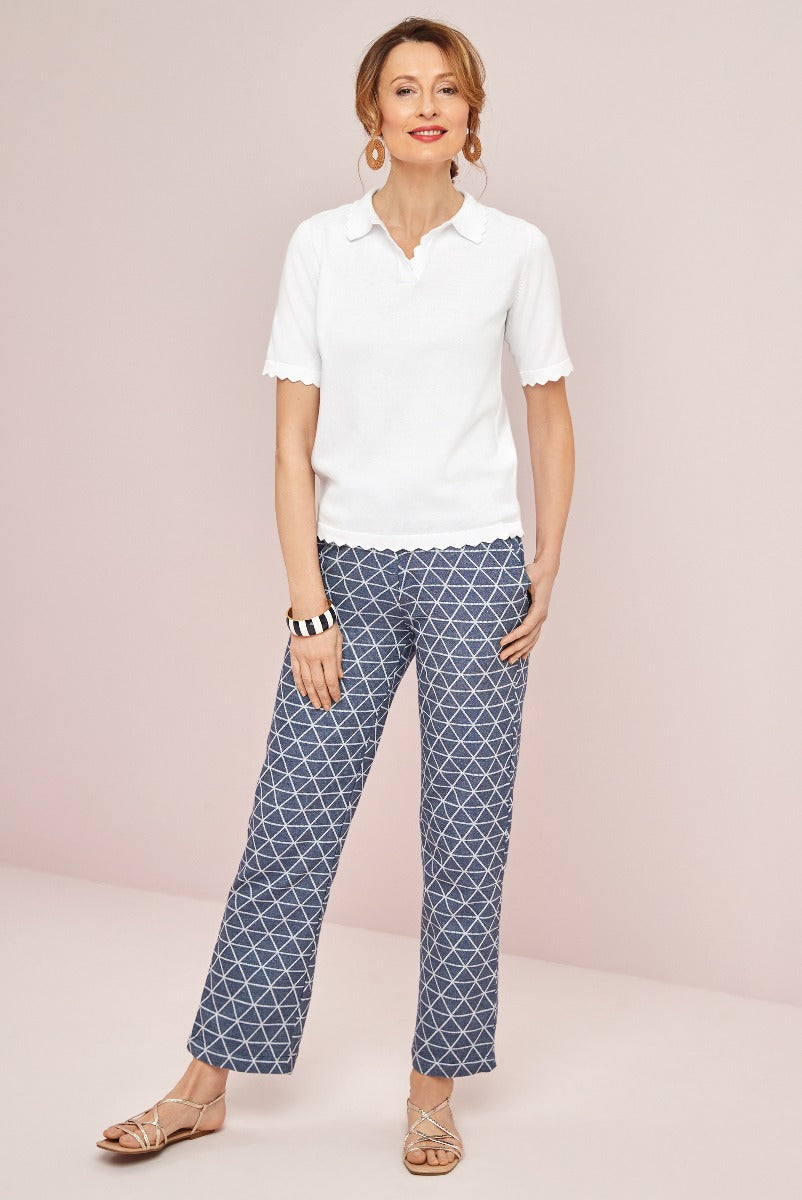 Lily Ella Collection model wearing classic white scalloped collar polo and chic geometric print trousers with elegant gold-strapped sandals, perfect for stylish casual wear.