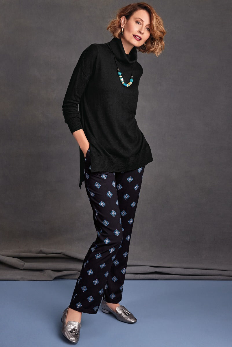 Lily Ella Collection elegant black cowl neck tunic sweater and patterned navy trousers, styled with silver loafers and a statement turquoise necklace, casual chic women's wear.