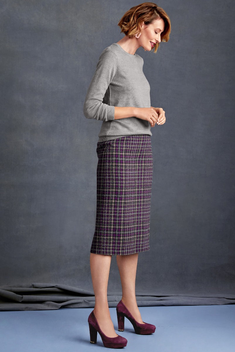 Elegant woman posing in Lily Ella Collection grey sweater and purple plaid pencil skirt, coordinating with purple high heels, stylish autumn-winter fashion, sophisticated office wear look