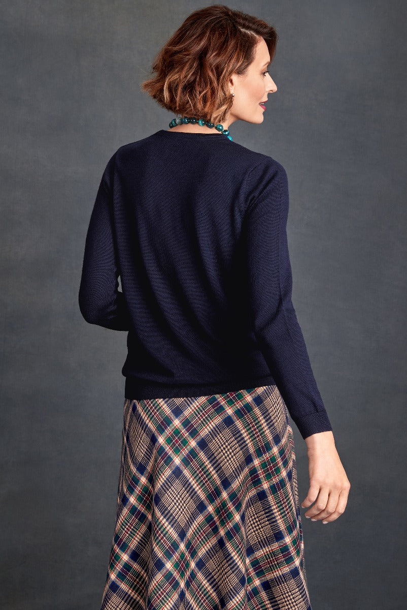 Lily Ella Collection Navy Blue Knit Jumper paired with Tartan Pleated Skirt, Fashionable Autumn Winter Outfit, Women's Elegant Casual Wear, Textured Top with Ribbed Cuffs and Hem, Profile View of Model Showcasing Back Details and Skirt Pattern
